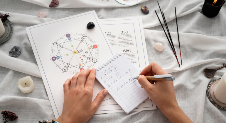 Person performing numerology calculations with a birth chart and spiritual tools on a table, including crystals, candles, and incense sticks.