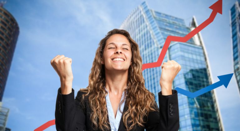 Happy businesswoman celebrating success with fists raised, standing in front of tall glass buildings with upward red and blue arrows, symbolizing accurate future predictions and growth through astrology.