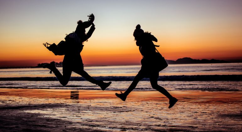 Two joyful individuals jumping on a beach during sunset, with a vibrant sky and ocean waves in the background, symbolizing happiness, freedom, and life prediction through astrology in India.